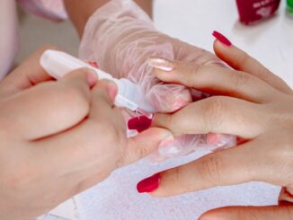 Hand mit roten Fingernägeln wird von einer Beautician gehalten und lackiert