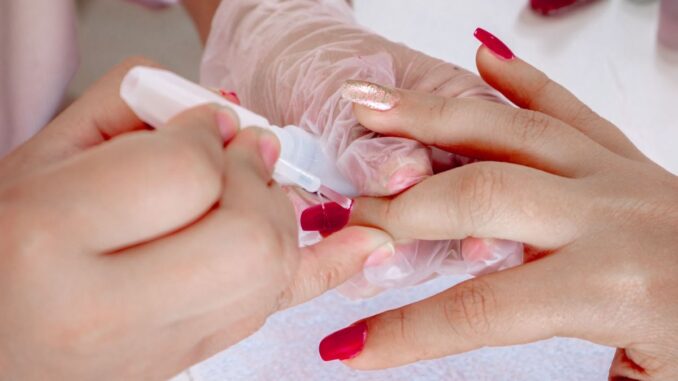 Hand mit roten Fingernägeln wird von einer Beautician gehalten und lackiert